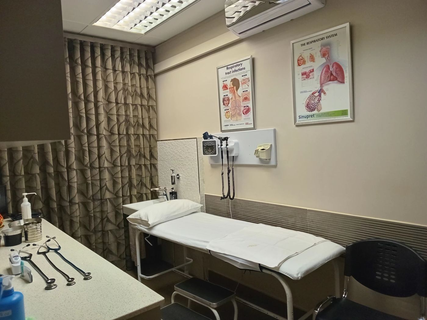 Dr Vawda's consulting room, with examination couch, wall-mounted examination instruments and a privacy curtain